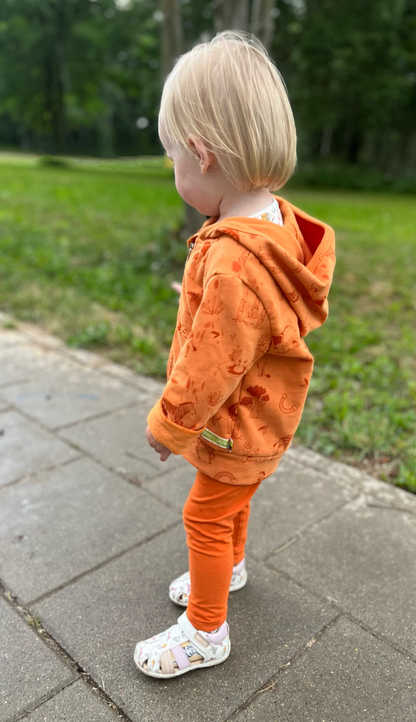 Ypatingai jaukus, lengvas ir minkštas vaikiškas GOTS organinės medvilnės džemperis su pūkeliu. Margintas žaismingu safari gyvūnų raštu. Orandžinės spalvos.