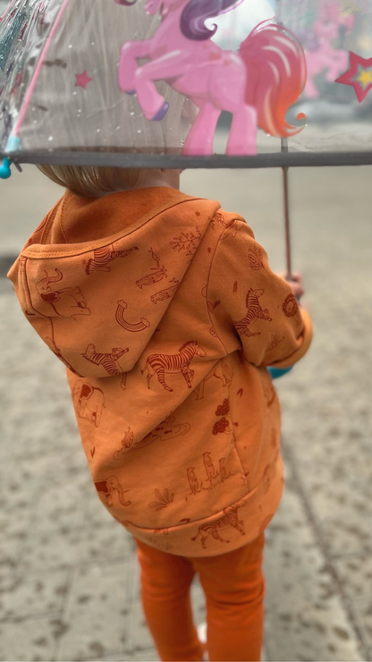 Ypatingai jaukus, lengvas ir minkštas vaikiškas GOTS organinės medvilnės džemperis su pūkeliu. Margintas žaismingu safari gyvūnų raštu. Orandžinės spalvos.